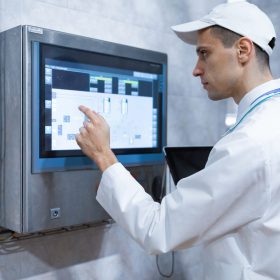 Technologist in a white coat with a laptop in his hands controls the production process on a digital screen in the dairy shop. Quality control at the dairy plant